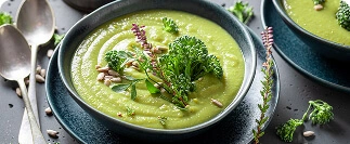 Green vegetable soup garnished with herbs and seeds in dark bowls