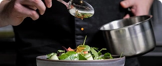 Chef drizzling dressing onto fresh salad greens in kitchen