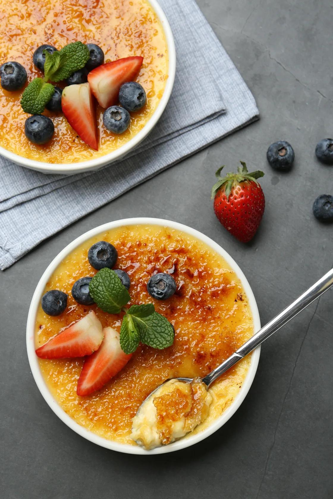 Two dishes of crème brûlée with berries and mint