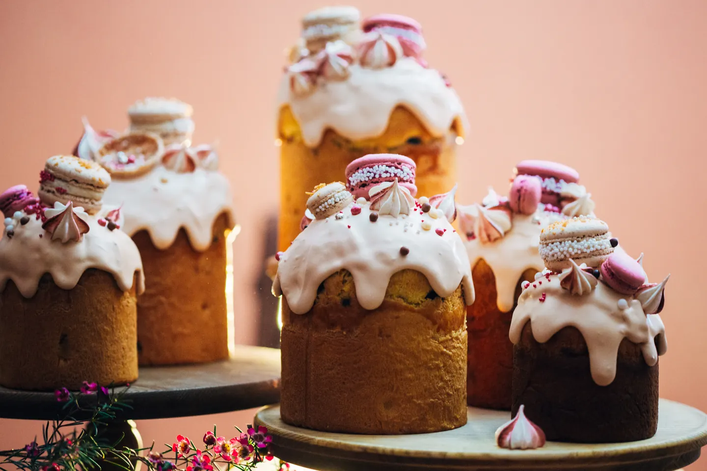 Iced celebration cakes decorated with macarons, meringues, and sprinkles on wooden cake stands.