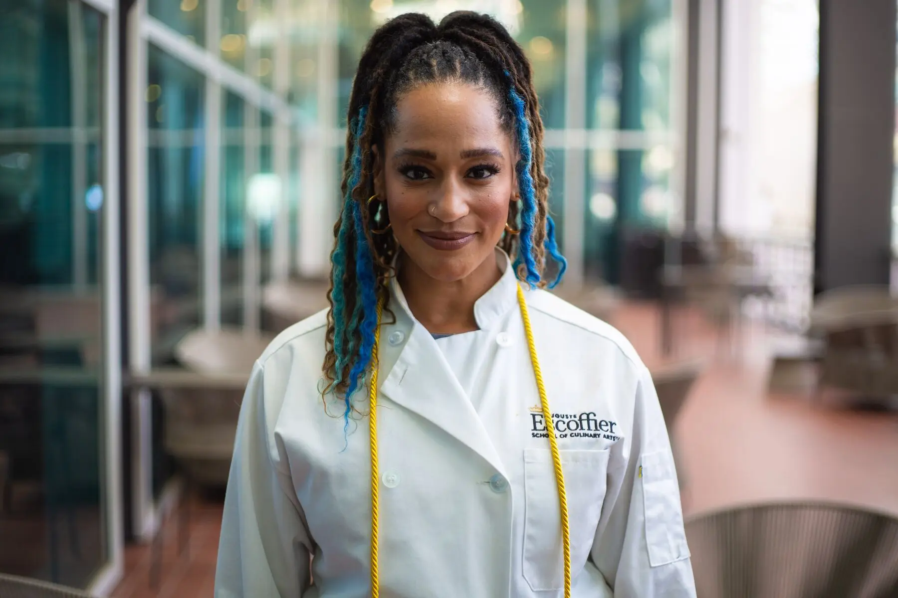 A smiling Escoffier student wearing a branded chef coat with a gold honor cord.