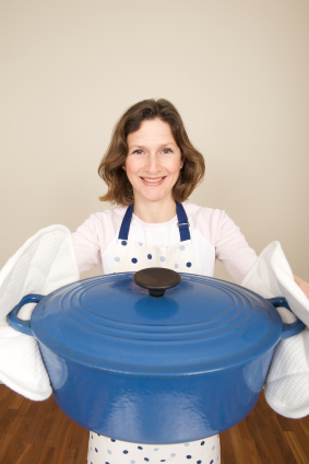 Woman offering a large blue cast iron casserole dish cooking pot