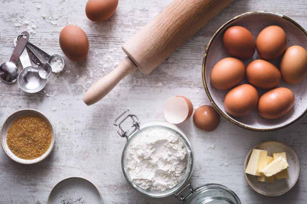 Flour, rolling pin, eggs, butter, and brown sugar on a table for a cake