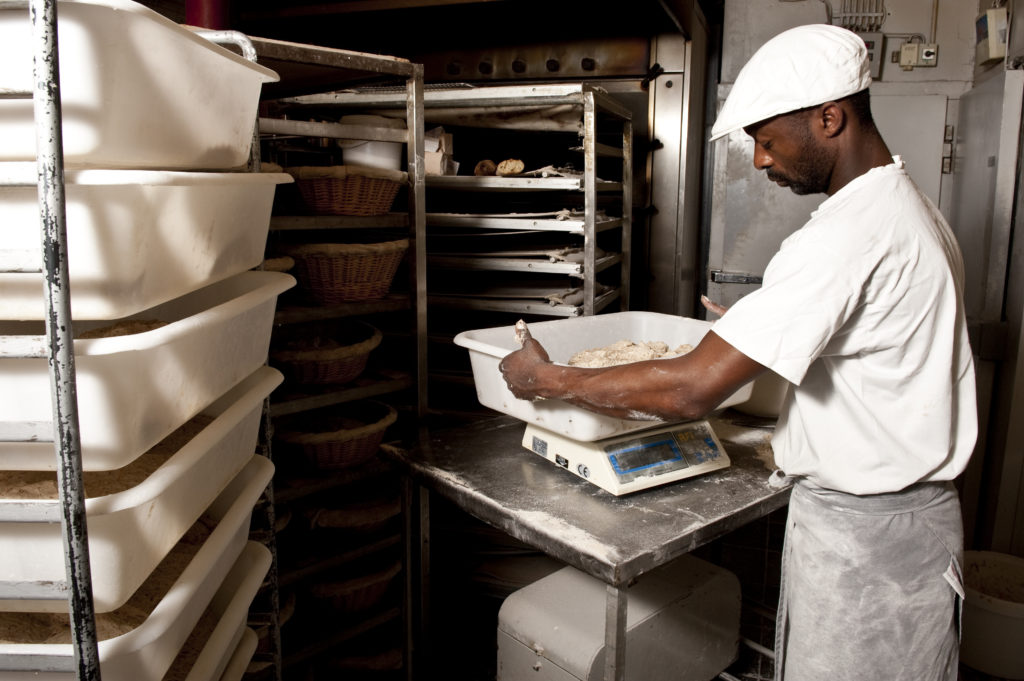 Male baker weighing dough on a scale