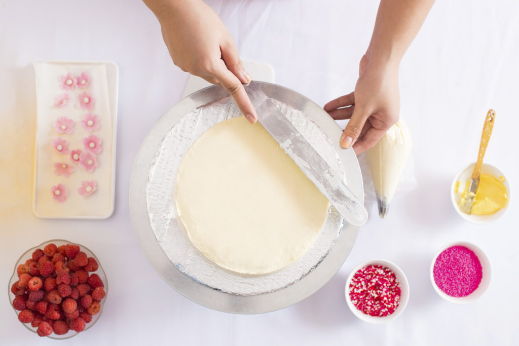 Putting frosting on a cake with raspberries, sprinkle as toppings