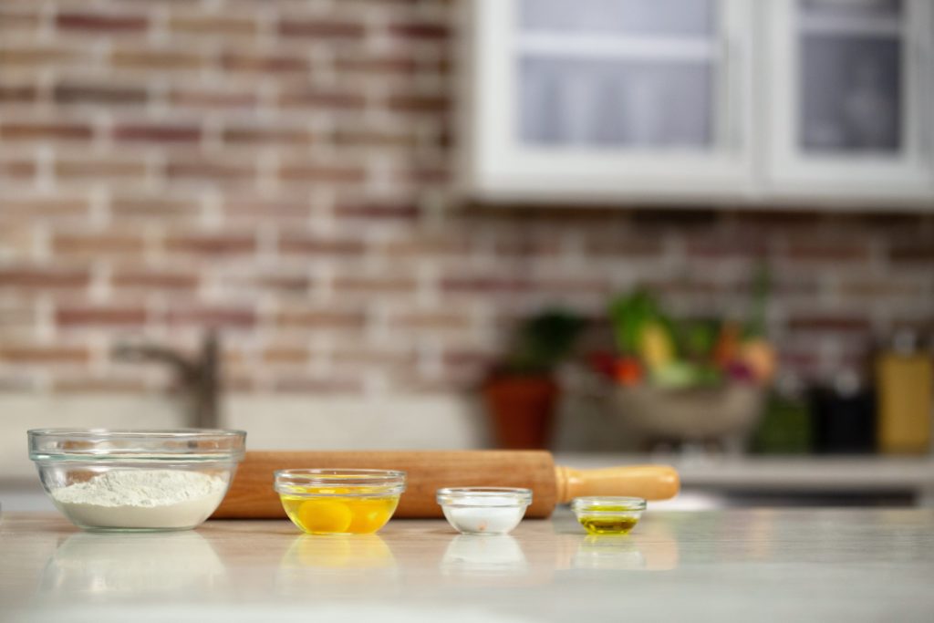 flour, eggs, sugar, oil in glass bowls and rolling pin 