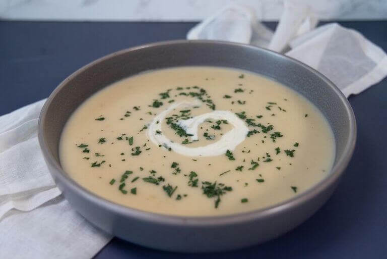A pureed potato soup garnished with a swirl of sour cream and finely chopped parsley fills a bowl.