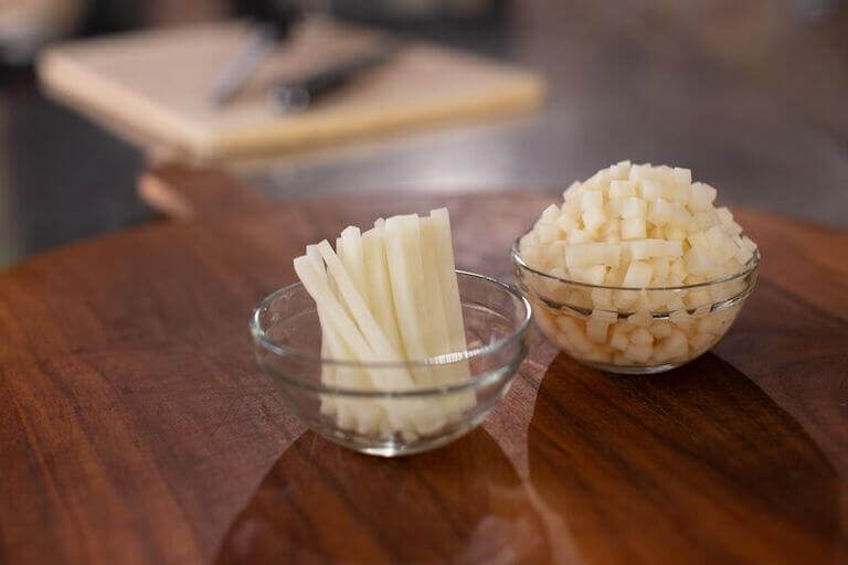 Two small glass bowls containing matchstick and cubed potatoes on a wooden surface.