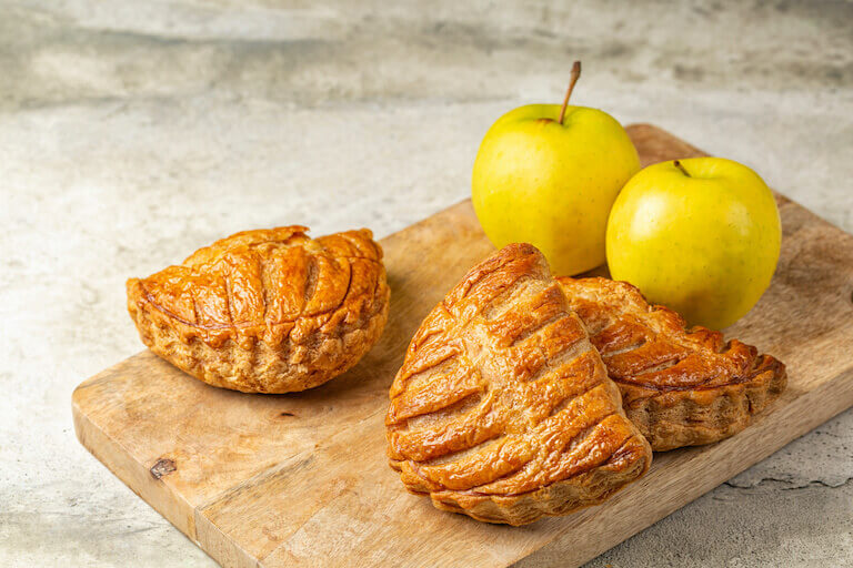 Apple turnovers next to apples on a wooden board