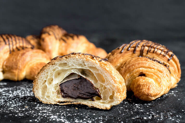 A chocolate croissant cut in half, revealing its rich, melted chocolate filling and flaky layers.
