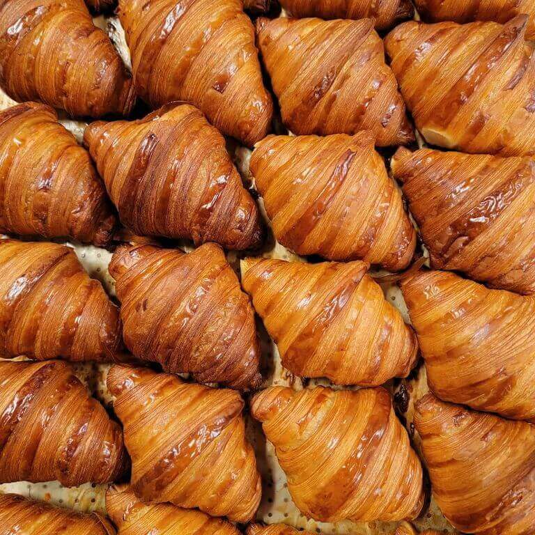 Rows of fresh croissants sitting on a tray