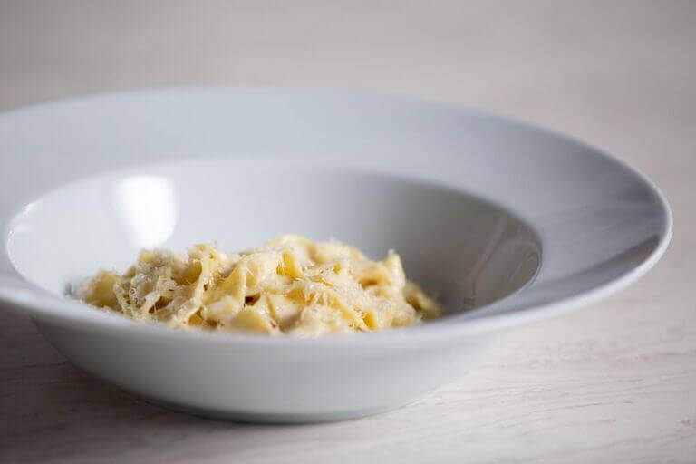 A white dish of fettuccine alfredo with shredded parmesan on top.