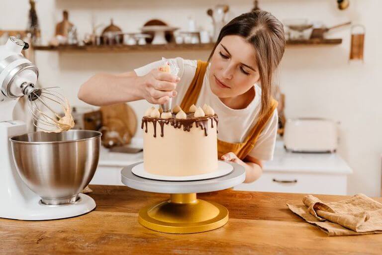 Pastry chef adding decoration to a brown cake on a golden cake stand