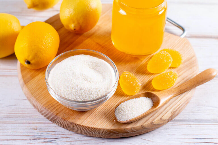 Pectin powder, jelly, and lemons sitting on a wooden board