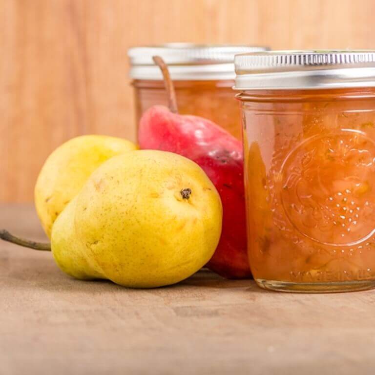 Two jars of jam sitting next to pears