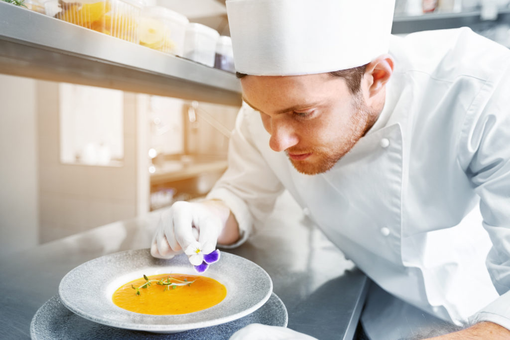 male chef cook serving and decorating plate of soup with flower at restaurant kitchen