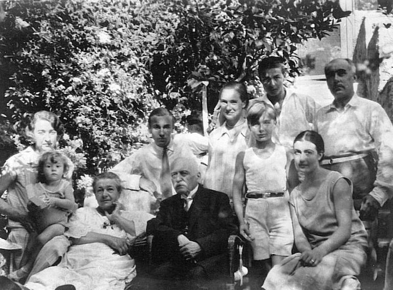 Escoffier sits in a garden, surrounded by several younger generations of his family.