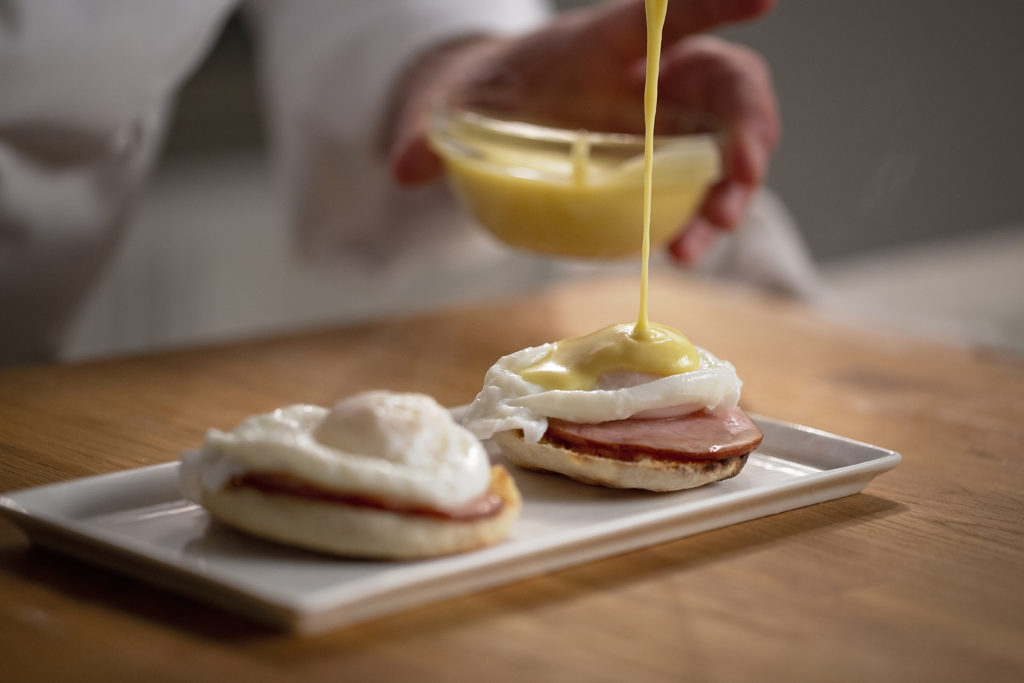 Adding hollandaise sauce to bagel egg and ham
