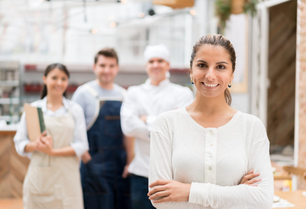 Smiling woman in white shirt standing in front of food workers