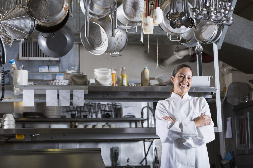 Female chef standing in commercial kitchen with pots and pans