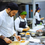 Male chef with black bandana cutting ingredients with knife in kitchen