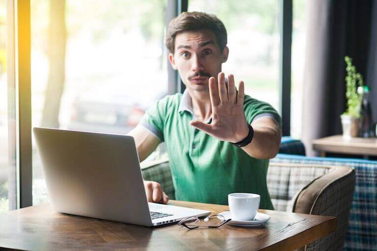 Person sitting at a table with a computer and coffee holding their hand up to signal stop