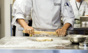 Escoffier pastry chef rolling flour dough in kitchen