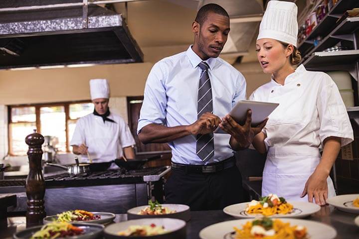 Restaurant manager in a tie showing chef an ipad in a kitchen