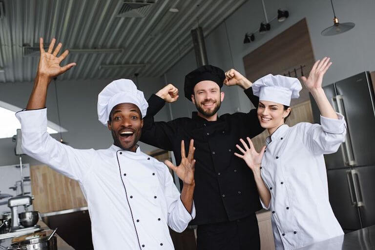 Three chefs smiling and celebrating in a kitchen