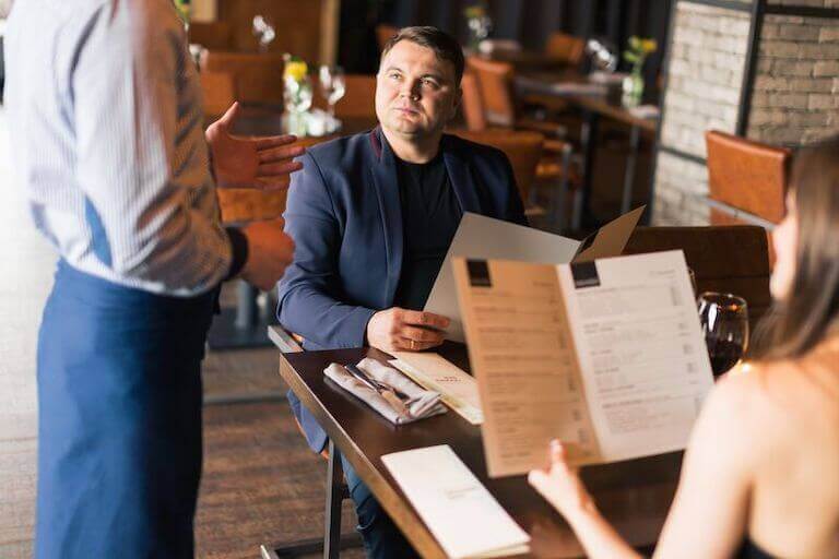 waiter talking to two guests seated at their table