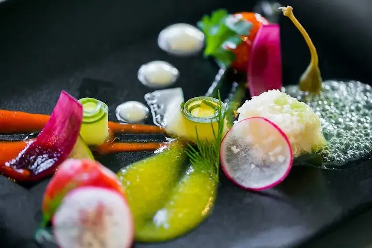 A plated molecular gastronomy dish featuring colorful spheres, airy foams, and intricate garnishes, showcasing innovative techniques that alter texture and presentation.