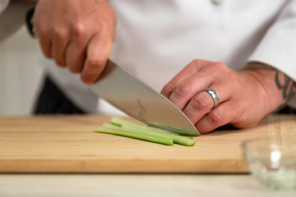 Chef cutting green vegetable using knife on a wooden board