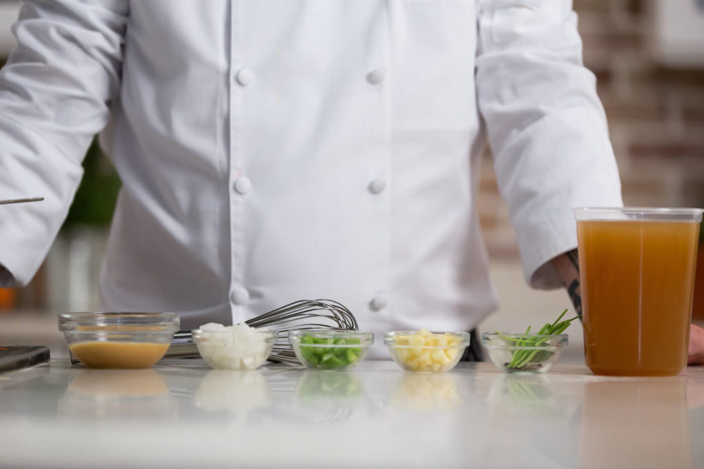 chopped onions, garlic and green peppers in a glass bowl in front of a whisk