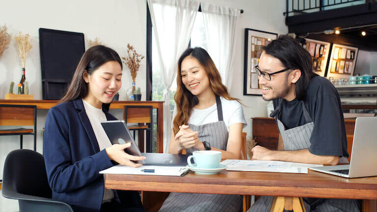 Business woman speaking with two cafe employees while looking at tablet