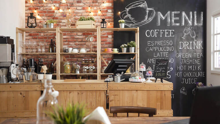 Front counter of a coffee shop with a menu written in chalk on a black wall