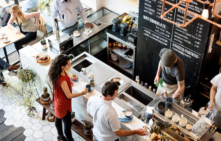 Two customers standing at a coffee bar drinking their coffee while and employee works behind the bar