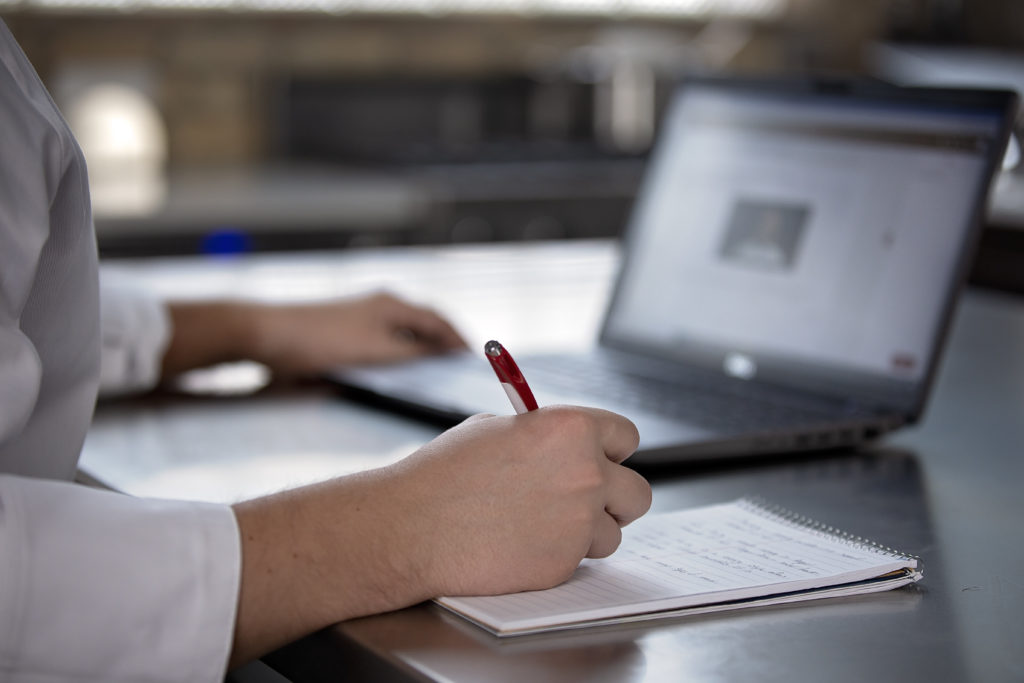 student taking notes on notepad with red pen while looking at computer