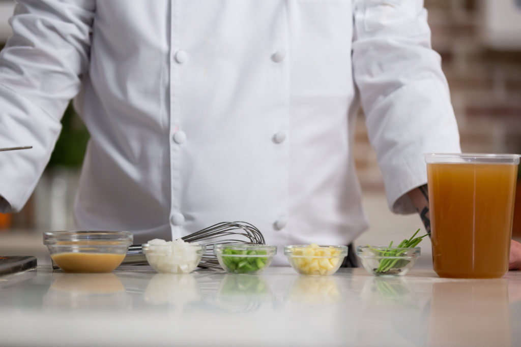 Chef in white chef's coat standing in front of condiments