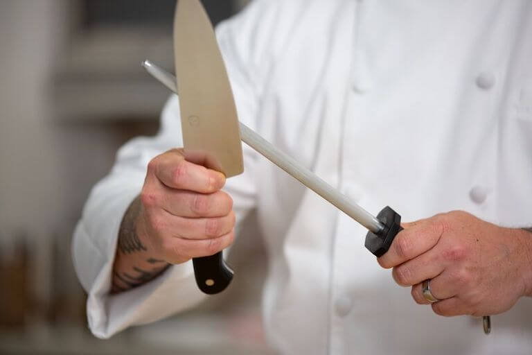 A chef in uniform sharpening their knife
