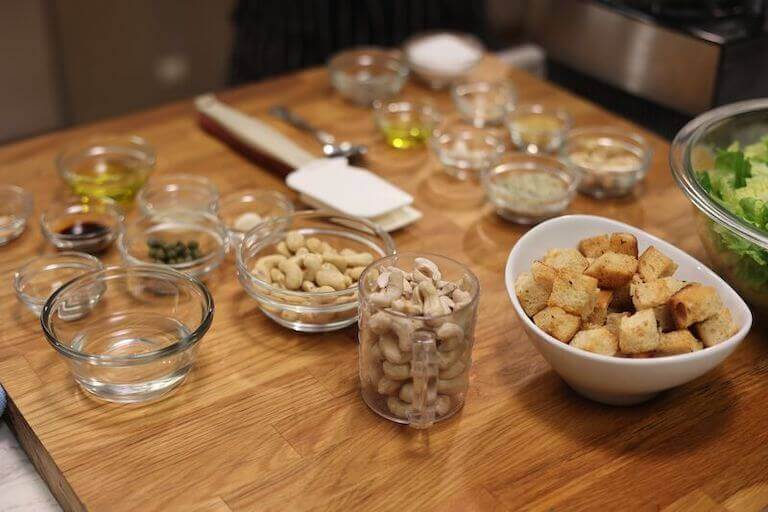 Cashews, lettuce, and other kale and romaine caesar salad ingredients separated into bowls