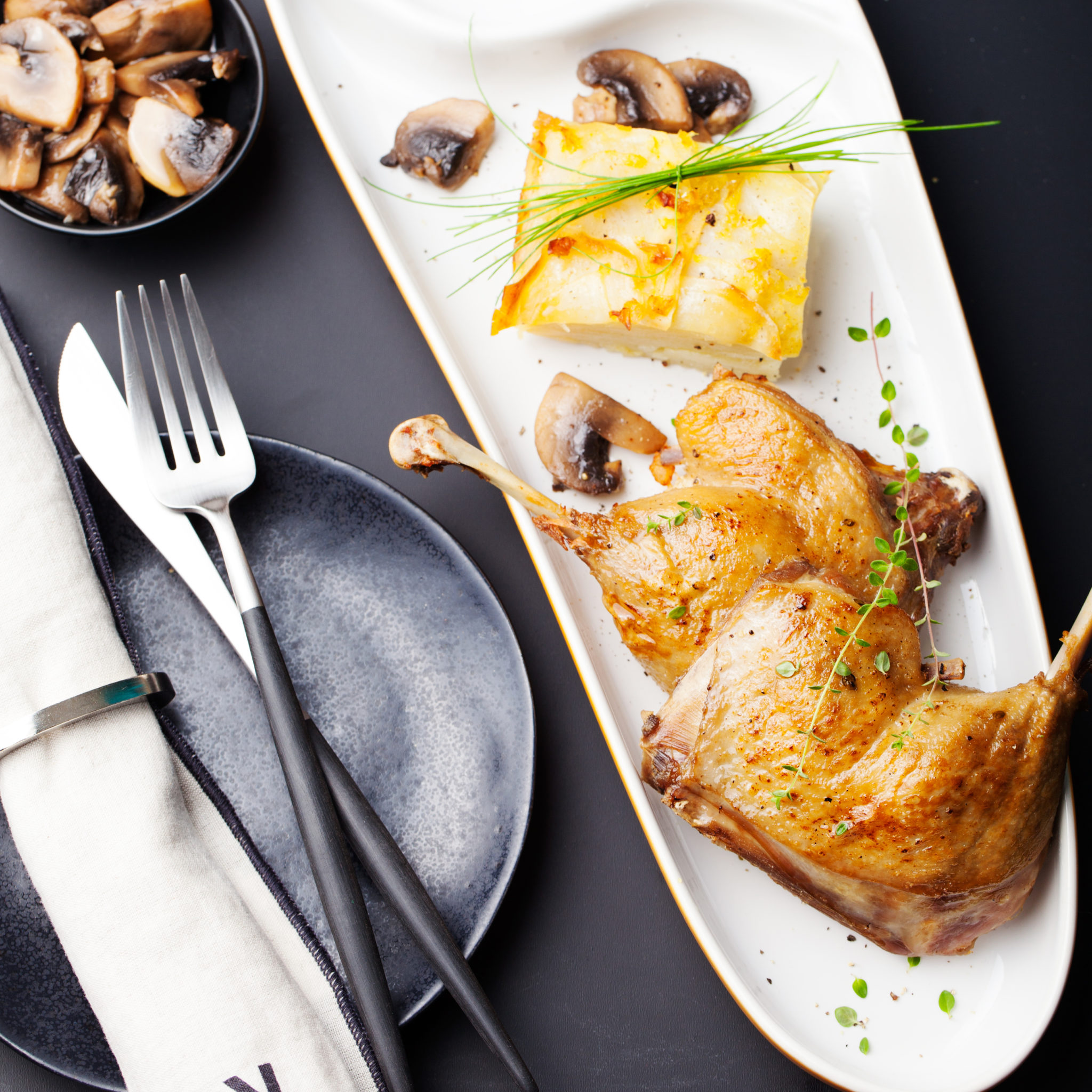 Duck legs confit with potato gratin and mushroom sauce .