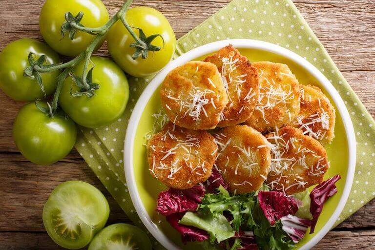 Bowl of fried green tomatoes and salad sitting next to a vine of tomatoes