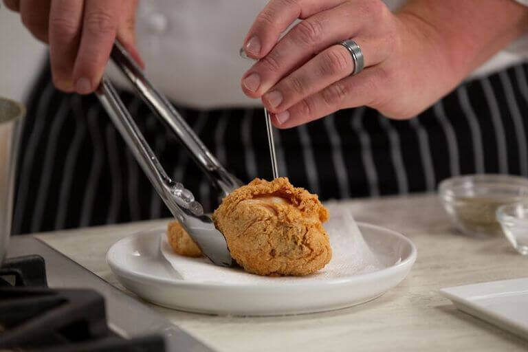 Chef holding fried chicken with metal tongs while checking its temperature