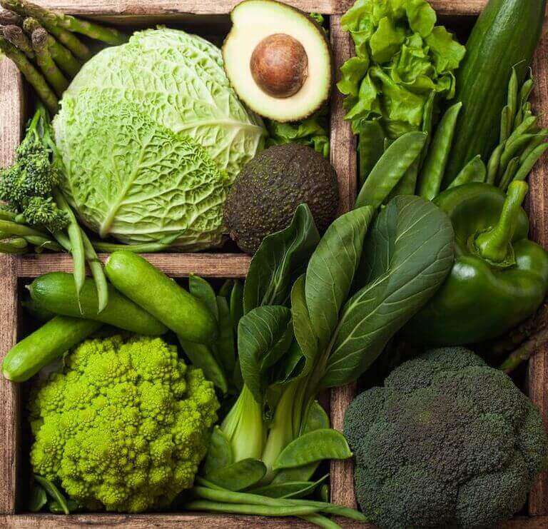 Lettuce, avocado, spinach, green peppers, and other green vegetables in a wood box