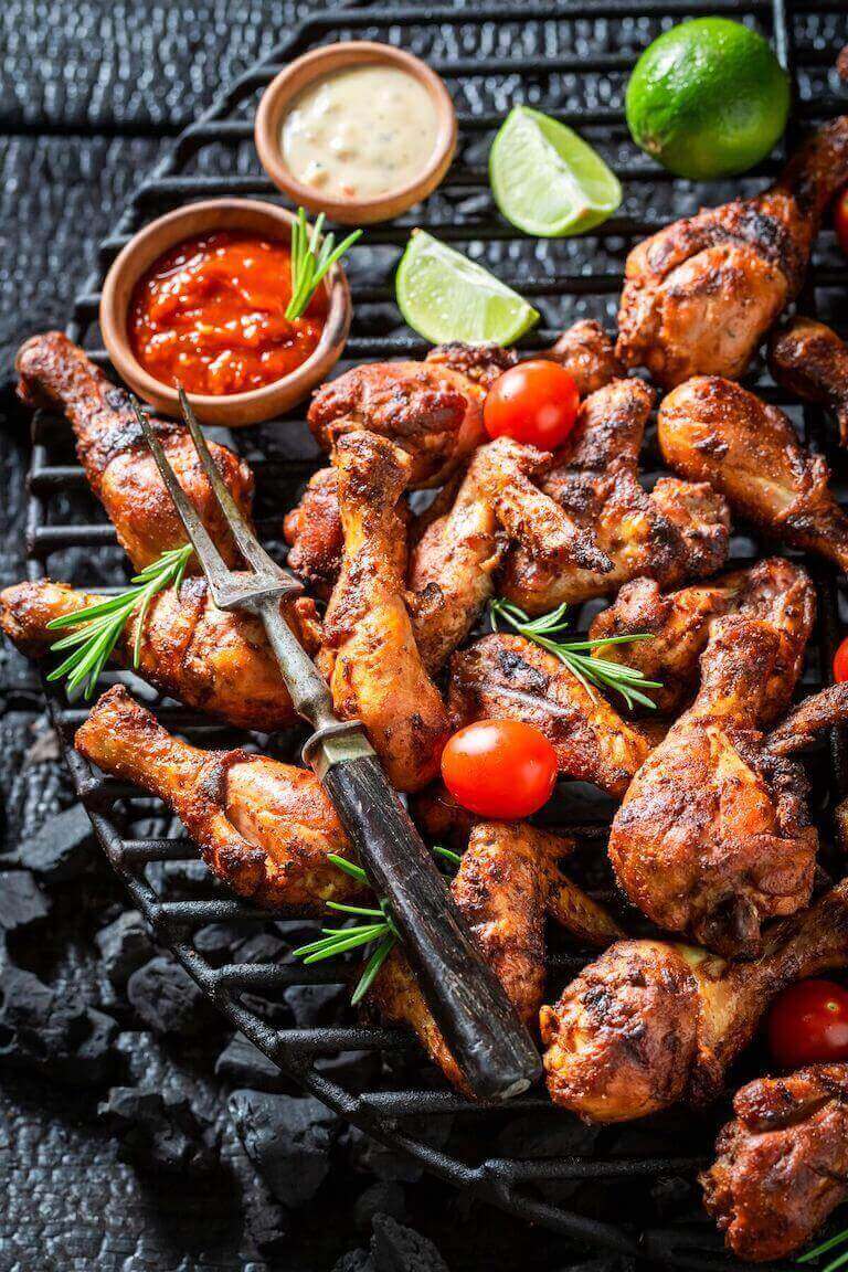 Roasted chicken wings on a grill with dipping sauces and limes