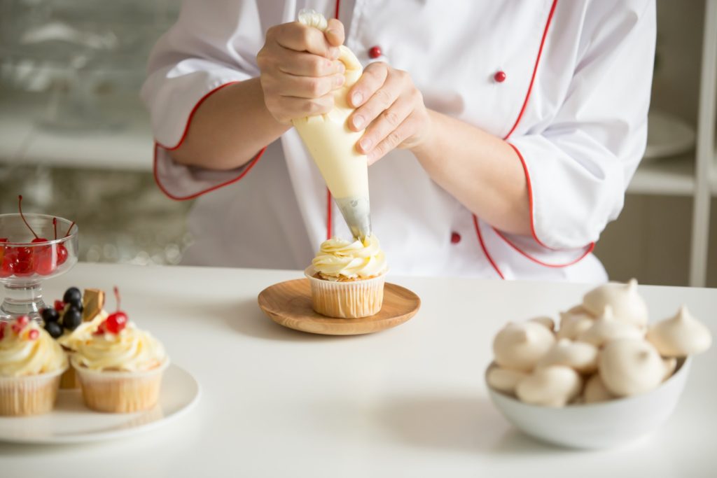 Chef piping icing on a cupcake