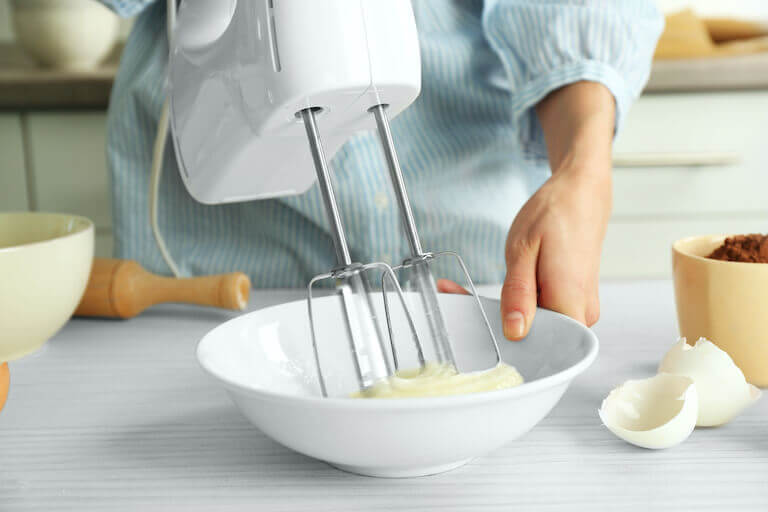 Close up of a chef mixing eggs in a bowl with a hand mixer