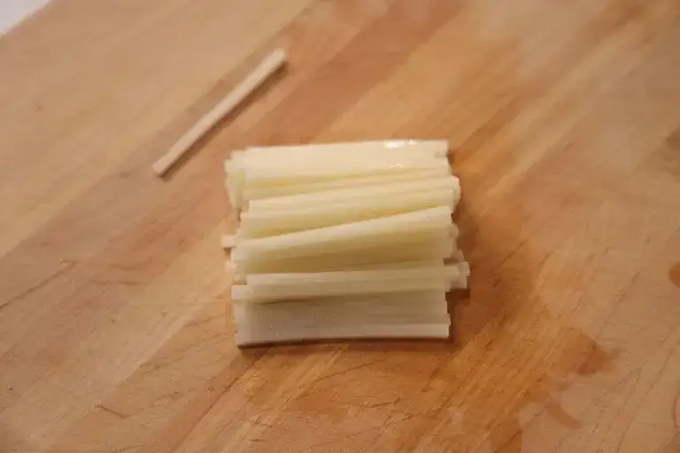 A stack of uniformly julienned white vegetables arranged neatly on a wooden cutting board to demonstrate consistent knife skills.