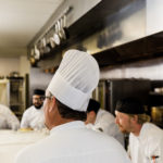 Chef talking to group of male cooks and culinary students in a kitchen