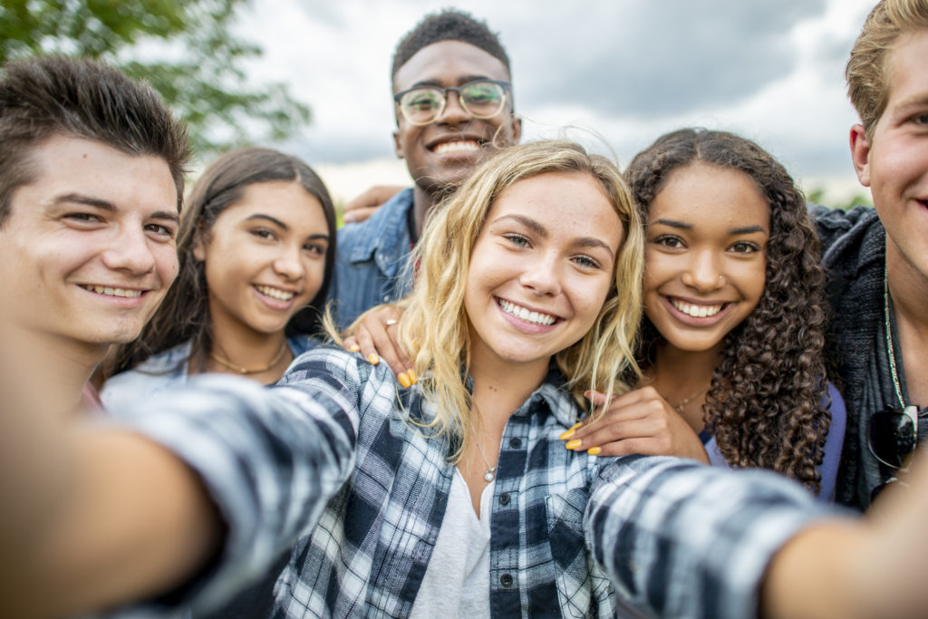 Smiling young teen boys and girls taking a group selfie